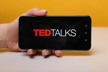 Person holding a phone with TED talks tech resources loading in the background